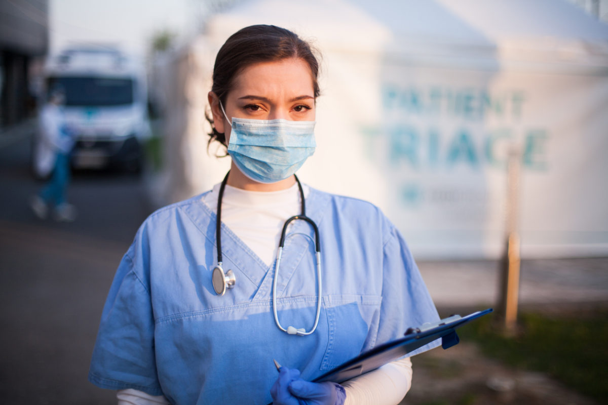 Crisis standards of care: Nurse in front of outdoor triage area.