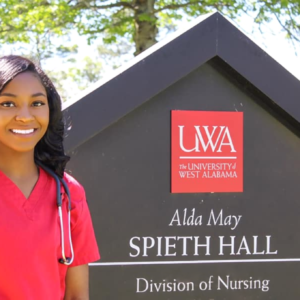 Student stands beside University of West Alabama Nursing Program sign.