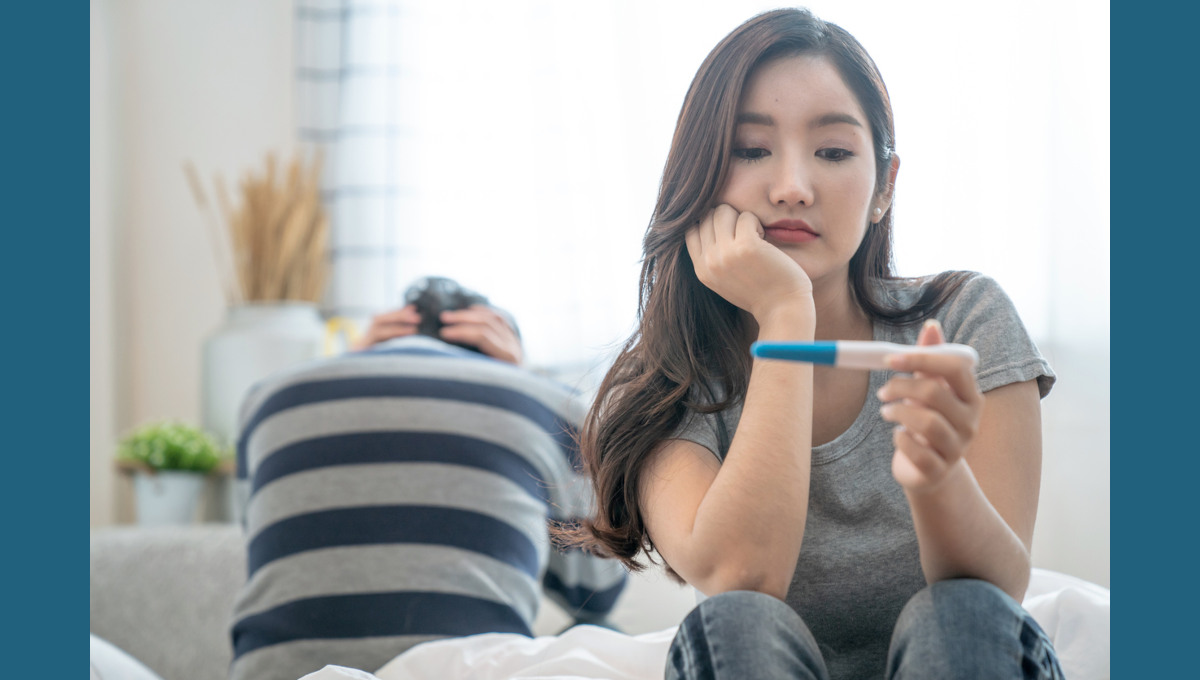 Concerned-looking young Asian American woman views results of pregnancy test.