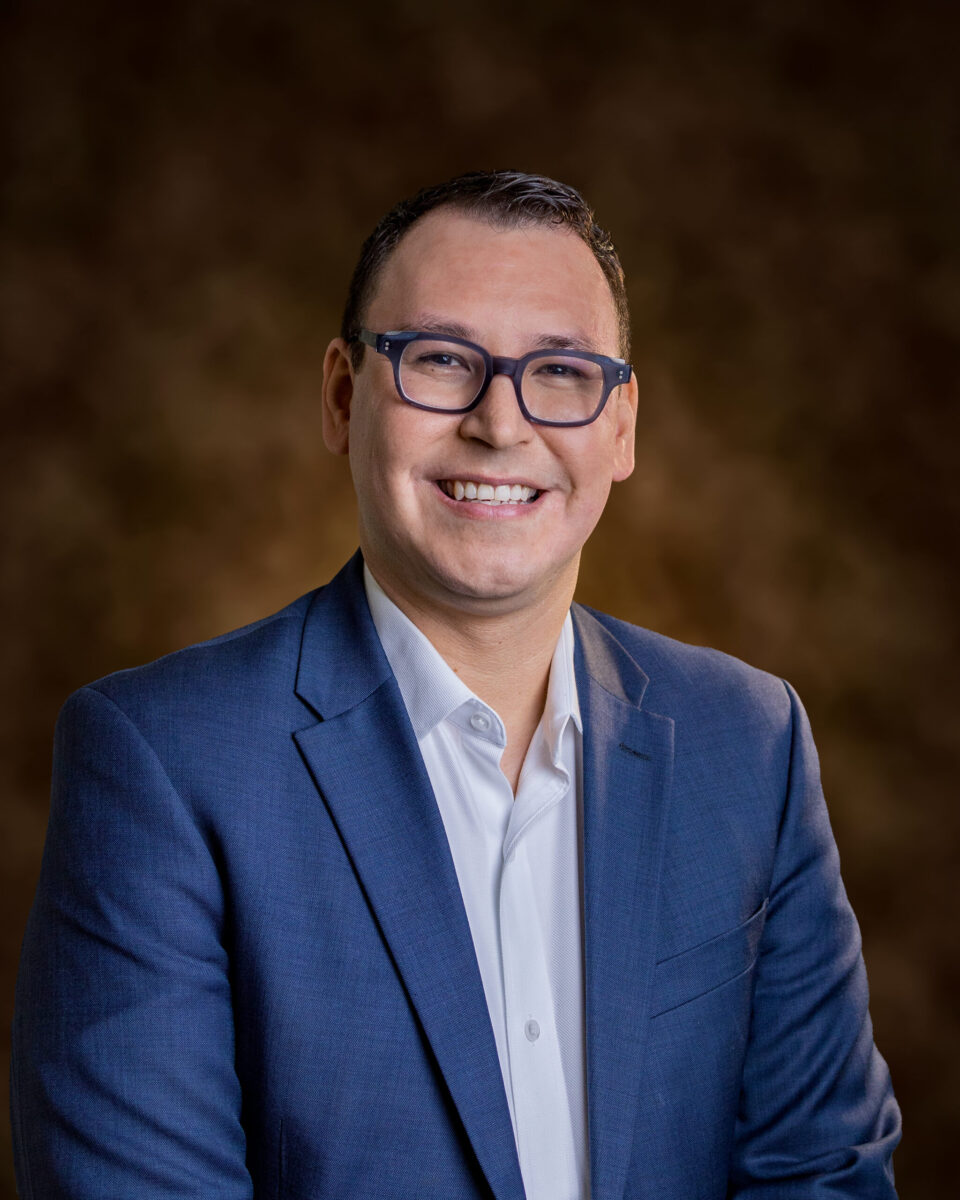 Oncology nurse Nick Escobedo in a blue button down shirt and a darker blue blazer