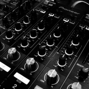 Black and white close-up of a DJ's audio mixing console with knobs and controls.
