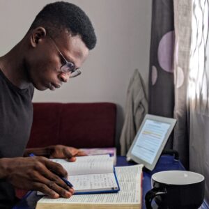 a young male at a table or desk with books and a coffee cup nearby studying to develop good study skills and study habits